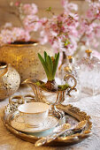 Silver tray with cup and saucer and hyacinth planted in sauce boat: cherry blossom in the background