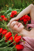 Top view of positive female lying in field with red tulip flowers and looking away