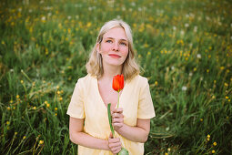 Smiling woman with red tulip in meadow