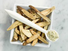 A bowl with licorice and a spoon with licorice root powder