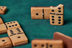 Sweet dominoes shaped cookies with black dots and bitten piece scattered on green surface