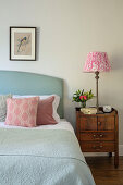 Bed with throw pillows and antique bedside table with lamp