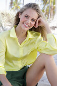 A young blonde woman wearing a yellow blouse and green shorts