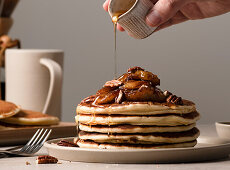 Hand pouring syrup over a plate of maple pecan pancakes with caramelized bananas