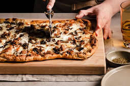 Hand slicing a mushroom, onion and sausage pizza on a cutting board