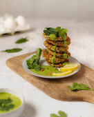 Herbal fritters stacked on plate and decorated with green sauce and lemon slice