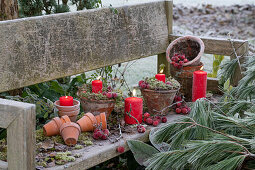 Weihnachtlich dekorierter Gartenbank mit Tontöpfen, roten Kerzen und Zieräpfeln