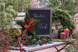 Stern aus Tannenzweigen, Ilexzweig und Schiefertafel mit Weihnachtgruß auf Gartenbank