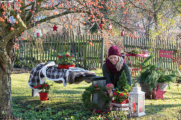 Woman decorating Christmas seat with lantern, mushrooms, and wreath in the garden