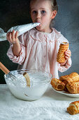 Little smilling girl is preparing puff pastry cream cones