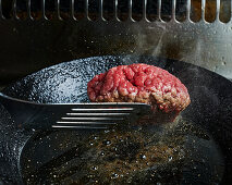 Beef burger patty in a frying pan being turned over