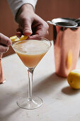 A whisky sour cocktail with lemon garnish being added to the glass