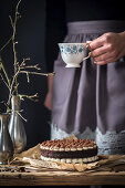 Tiramisu cake with a woman in the background holding a cup of coffee