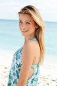 Young blonde woman in palm print dress near the sea