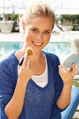 Blonde woman in blue shirt applying makeup with brush