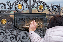 Frau berührt das bronzene Relief des Hl. Johannes von Nepomuk auf der Karlsbrücke, Prag, Tschechien