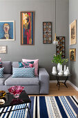 Grey upholstered sofa with cushions, next to it side table with vase collection and artwork on grey wall