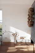 Floor vase with twigs and stool in the sunlit room, wreath of honeycomb paper balls on a fireplace wall