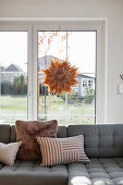 Grey upholstered sofa with cushions in front of patio door with star decoration hanging from it