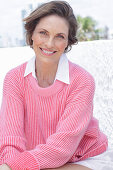 Frau in pinkfarbenem Pullover und weißem Hemd am Strand