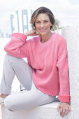 A woman wearing a pink jumper and white trousers
