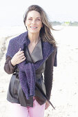 Long-haired woman in a dark coat with a sweater over her shoulders on the beach