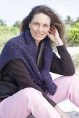 Long-haired woman in a dark coat with a sweater over her shoulders on the beach