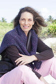 Long-haired woman in a dark coat with a sweater over her shoulders on the beach