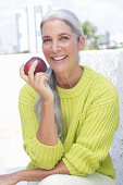 Grauhaarige Frau mit einem Apfel in grüngelbem Strickpullover