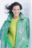 Reife, dunkelhaarige Frau in grünem Mantel und grüngelbem Strickpullover