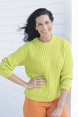 Mature, dark-haired woman in a green and yellow knit sweater and orange pants