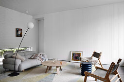 Grey upholstered sofa with coffee table and chairs in living room with white walls