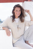 A happy, long-haired woman wearing a light, casual knitted jumper and trousers
