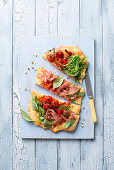 Pinsa with roasted peppers, tomatoes, parma ham, basil and rocket