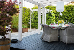 Pergola with glass roof, rattan chairs around table on wooden platform