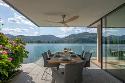 Esstisch auf überdachter Terrasse mit Glasbrüstung und Seeblick