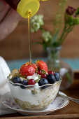 Joghurt mit Birnen, Haferflocken, Kürbiskernen und frischen Beeren wird mit Honig beträufelt