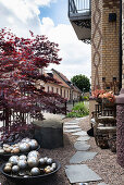 Garden path with slate slabs in gravel, bowls with silver balls, Japanese maple, and granite block shaped boulder