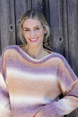 Young blonde woman in a knitted jumper with a colour gradient in front of a board wall