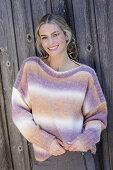 Young blond woman in knitted jumper with colour gradient in front of board wall