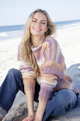 Young blonde woman in a knitted jumper with a colour gradient and jeans by the sea