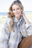 Young blonde woman in a checked coat and suede trousers by the sea