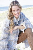 Young blonde woman in checked coat and suede trousers by the sea
