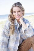 Young blonde woman in checked coat and suede trousers by the sea