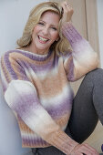 Mature blonde woman in knitted jumper with colour gradient and grey leggings