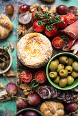 Snack board with cheese, jamon serrano, fuet, buns, olives, cherry toamtoes, grapes, walnuts and capers