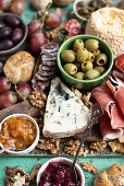 Cheese and meat board with cheese, Serrano ham, fuet, bread, olives, tomatoes, grapes, nuts, and jam