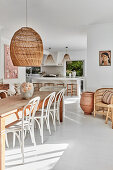 Rustic wooden dining table with white chairs, rattan lamp above in open living area
