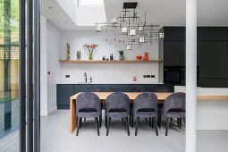 Esstisch aus Holz in Verlängerung zur Kücheninsel und elegante Polsterstühle in offenem Wohnraum