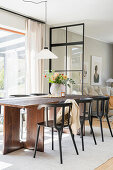 Dining area with a wooden table in front of a window, with an industrial style glass paneled wall as room divider